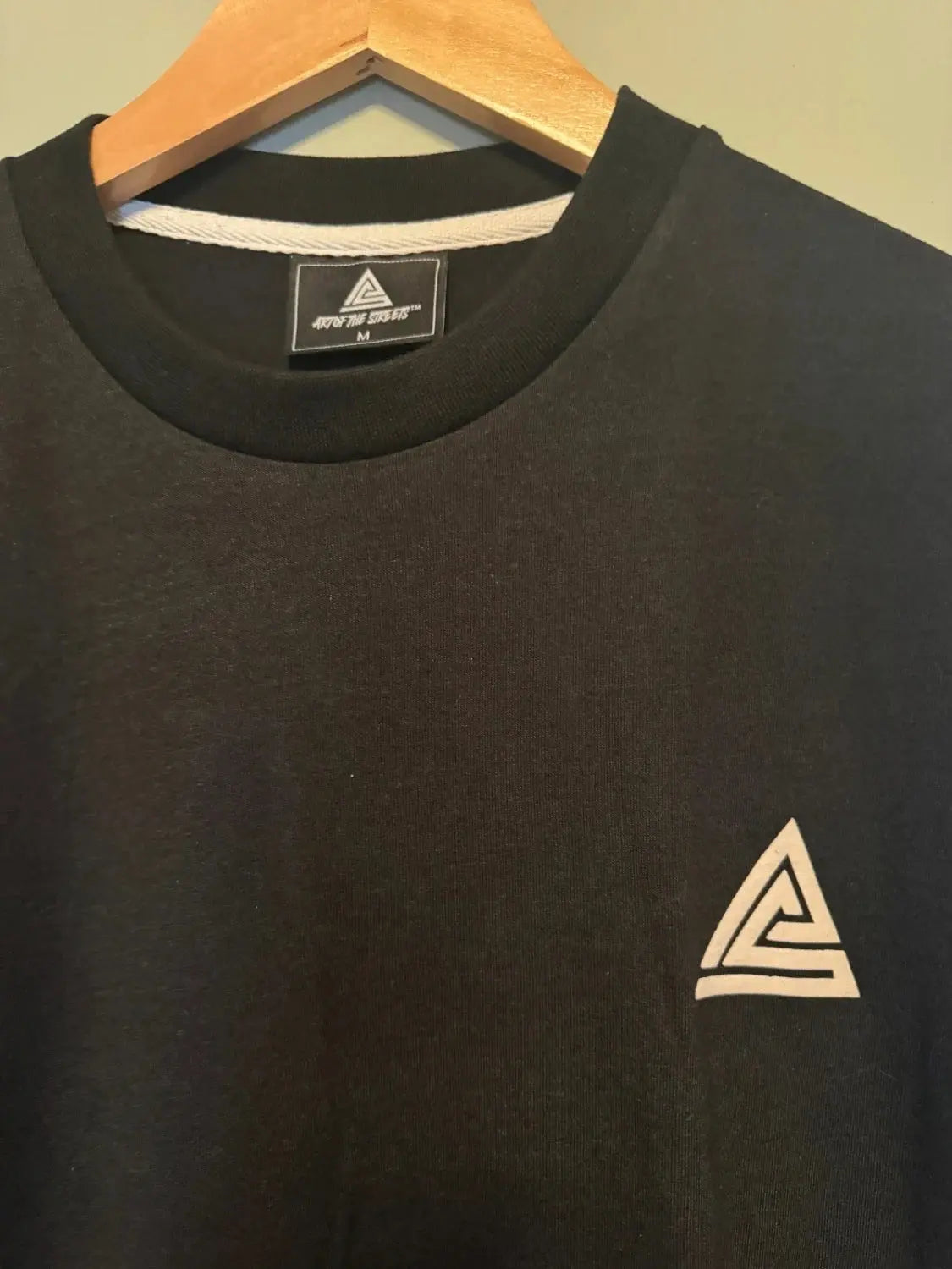T-shirt noir, de AOTS, avec un logo triangulaire blanc sur la poitrine et un col rond.