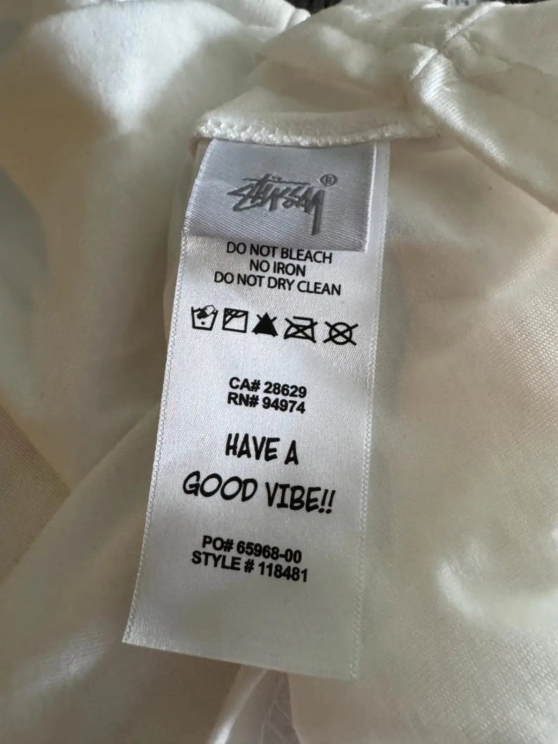 Étiquette d'entretien d'un t-shirt blanc par Stüssy avec instructions de lavage et message "Have a good vibe!!".
