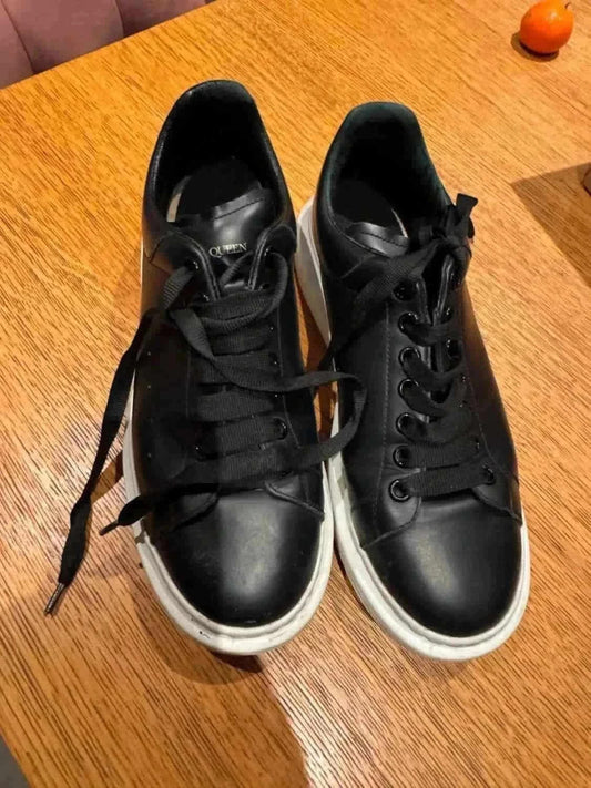 Baskets noires en cuir par Alexander McQueen, avec des lacets noirs et semelles blanches épaisses.