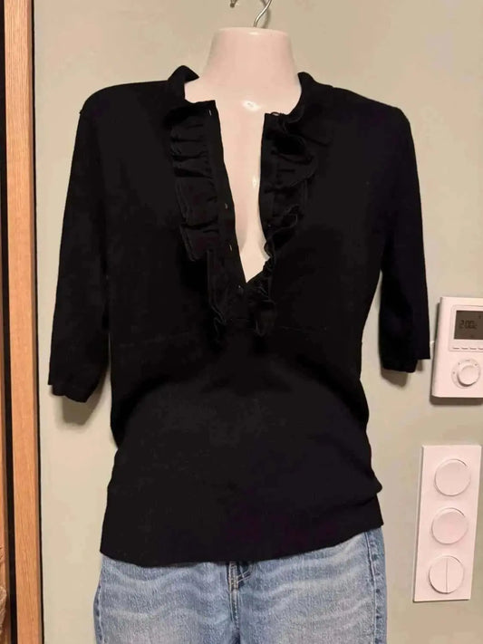 Blouse noire à manches trois-quarts de Kookai, avec des volants décoratifs sur le devant et portée avec un jean.
