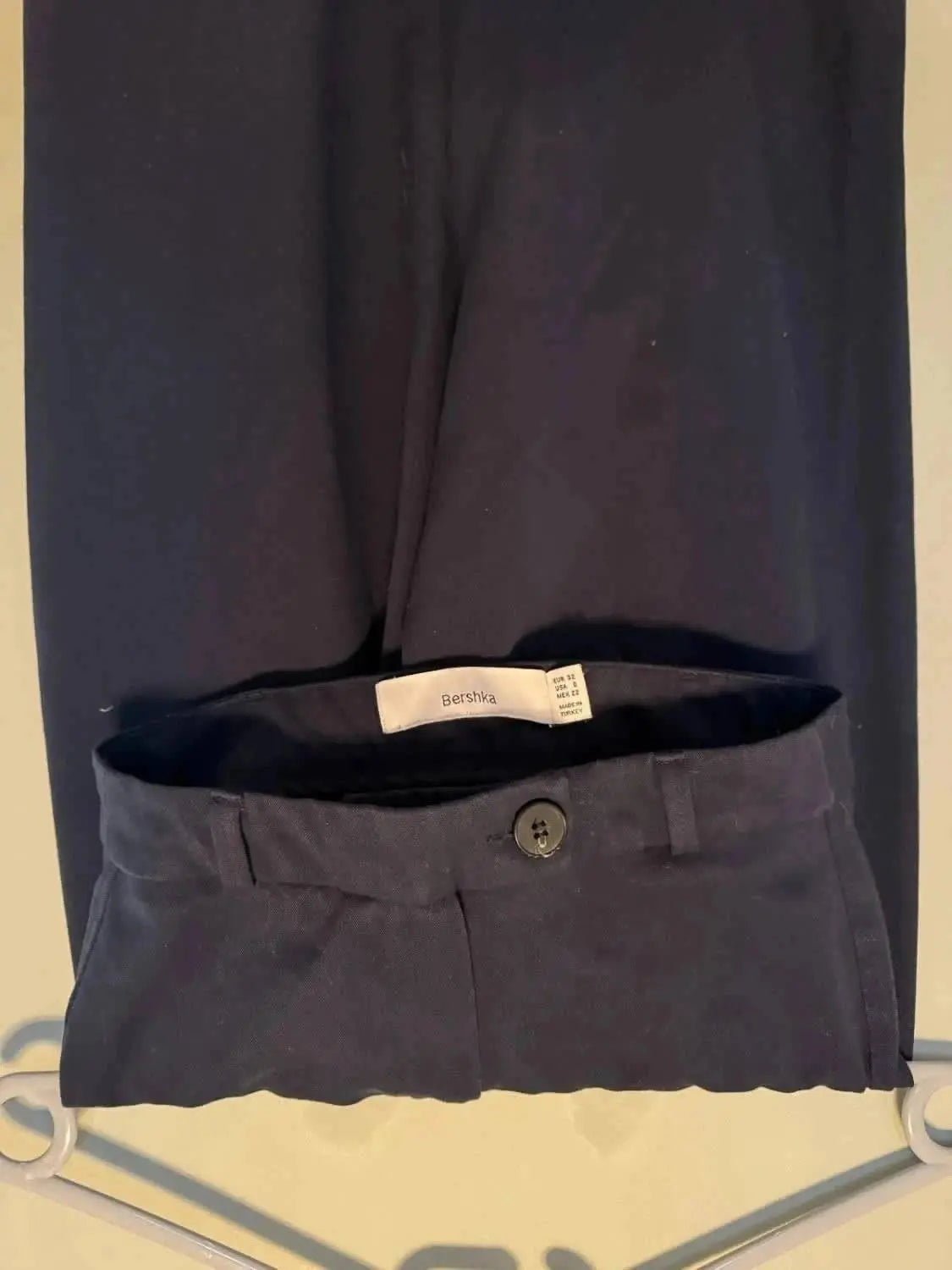 Pantalon bleu marine de Bershka, avec une taille à bouton et une étiquette de la marque visible.
