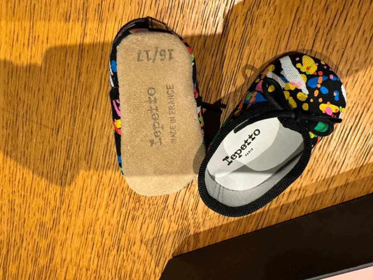 Chaussons ballerines pour bébé noir et multicolore de Repetto, avec motifs peints et nœud décoratif.
