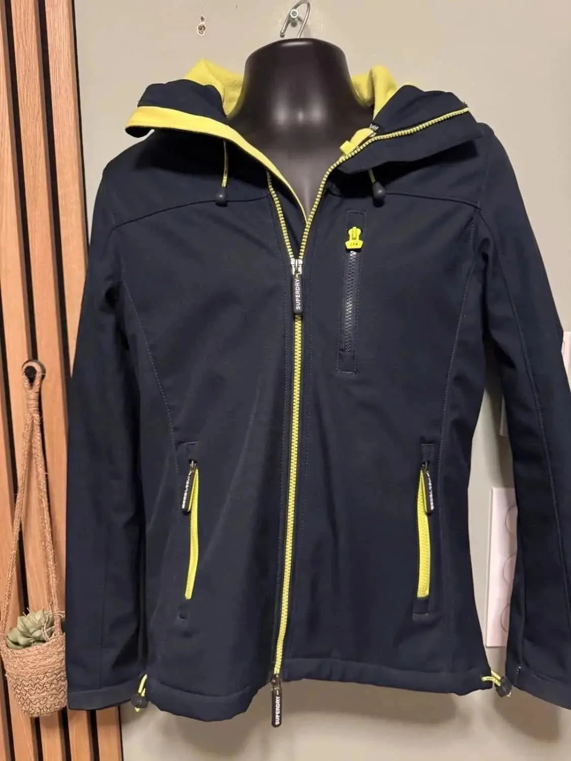 Veste Windtrekker noire de Superdry avec détails jaunes, capuche doublée et fermeture éclair.