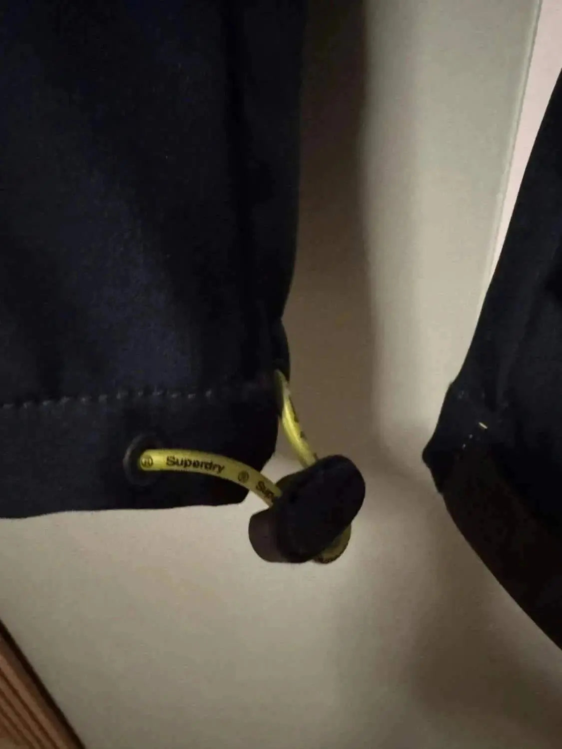Veste Windtrekker noire de Superdry avec cordon jaune.