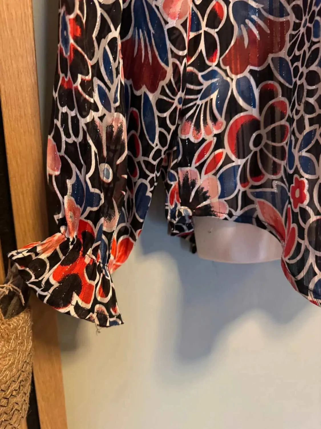 Blouse fluide imprimée par Nina Kaufmann, à motifs floraux rouge, bleu et noir, avec des détails métalliques brillants.
