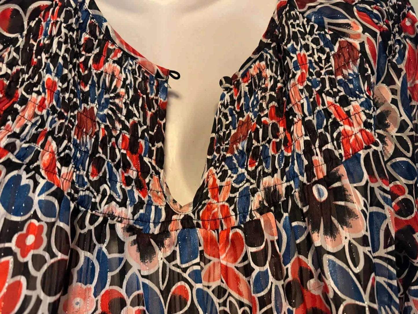 Blouse fluide imprimée par Nina Kaufmann, avec motifs floraux rouges, bleus et noirs et détail smocké à l'encolure.

