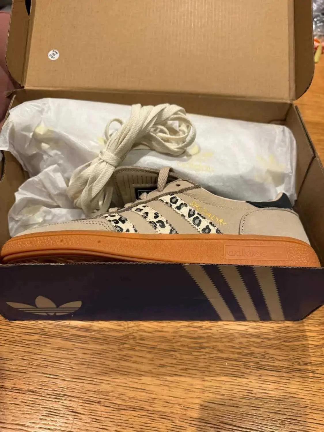 Chaussure de handball beige et léopard, de Adidas, avec semelle en gomme et lacets écrus.

