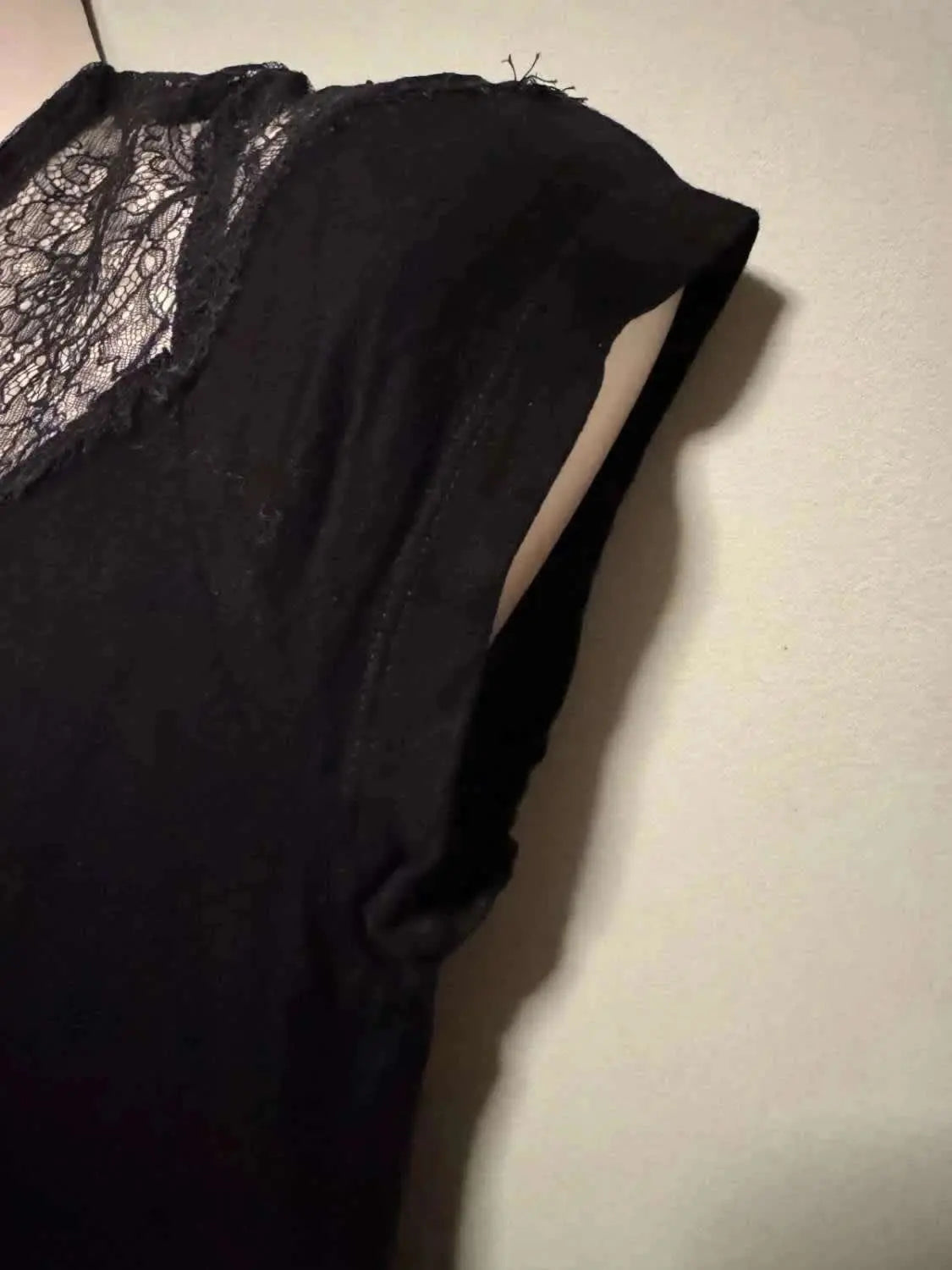Haut noir de Maje avec empiècement en dentelle florale sur l'épaule et le décolleté.

