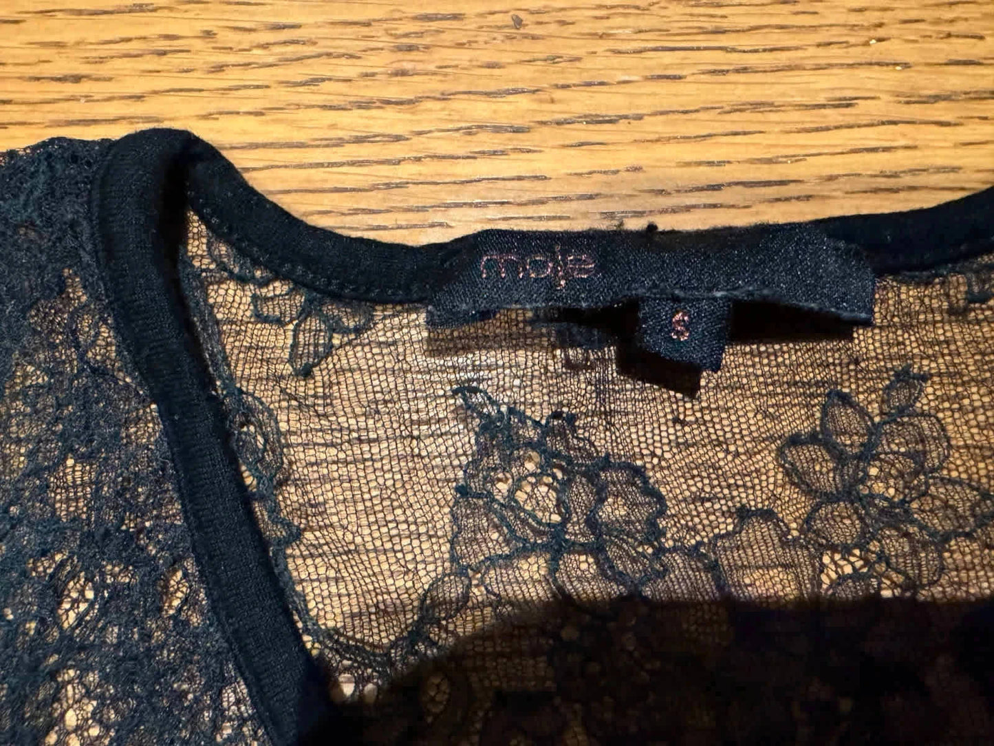Haut noir en dentelle de Maje, avec étiquette de taille visible, sur un fond en bois.

