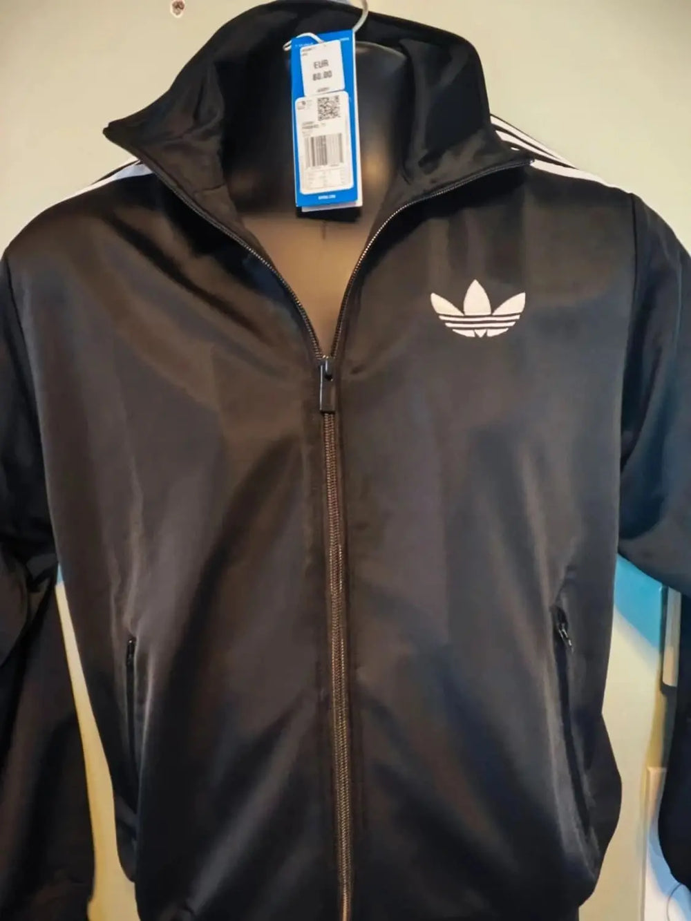 Veste de survêtement noire par Adidas Originals avec fermeture éclair sur le devant et logo trèfle blanc.