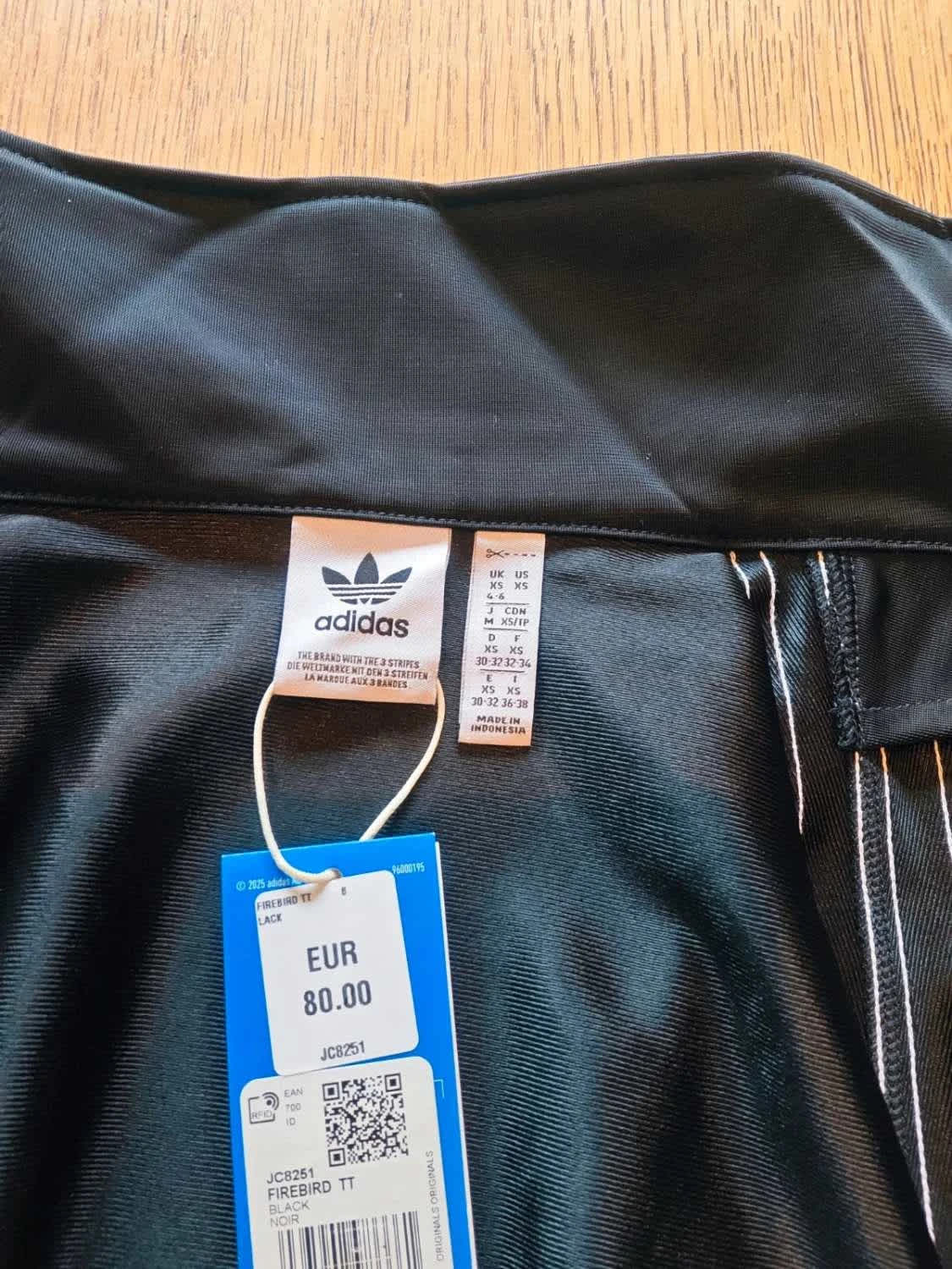 Veste de survêtement noire Firebird TT par Adidas Originals avec les trois bandes blanches sur le côté.