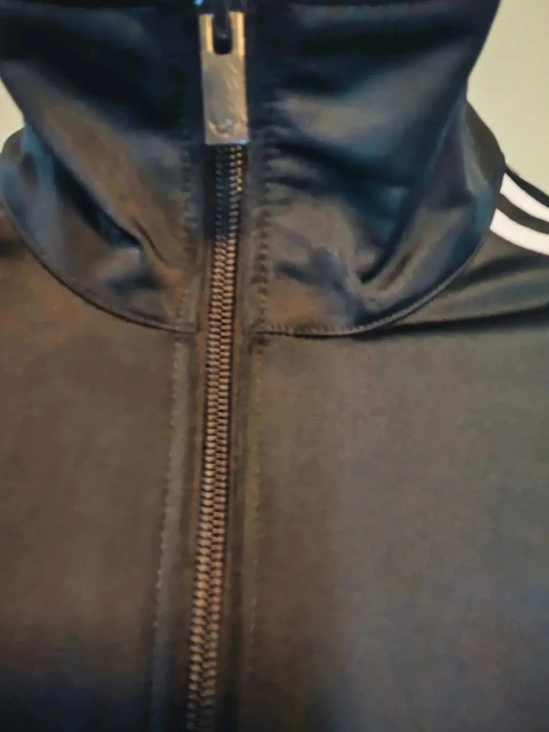 Veste de survêtement noire Adidas Originals avec fermeture éclair et les trois bandes blanches sur l'épaule.
