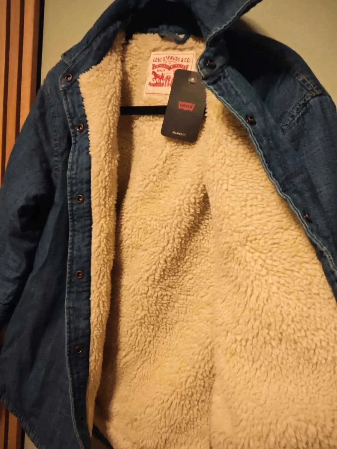 Veste en jean doublée sherpa de Levi's, avec étiquette noire, sur un cintre.