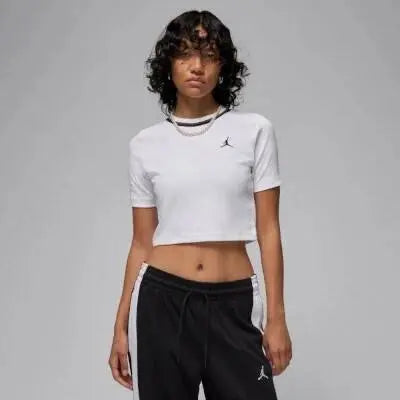 Crop top blanc de Jordan avec un petit logo sur la poitrine, porté avec un pantalon de survêtement noir.
