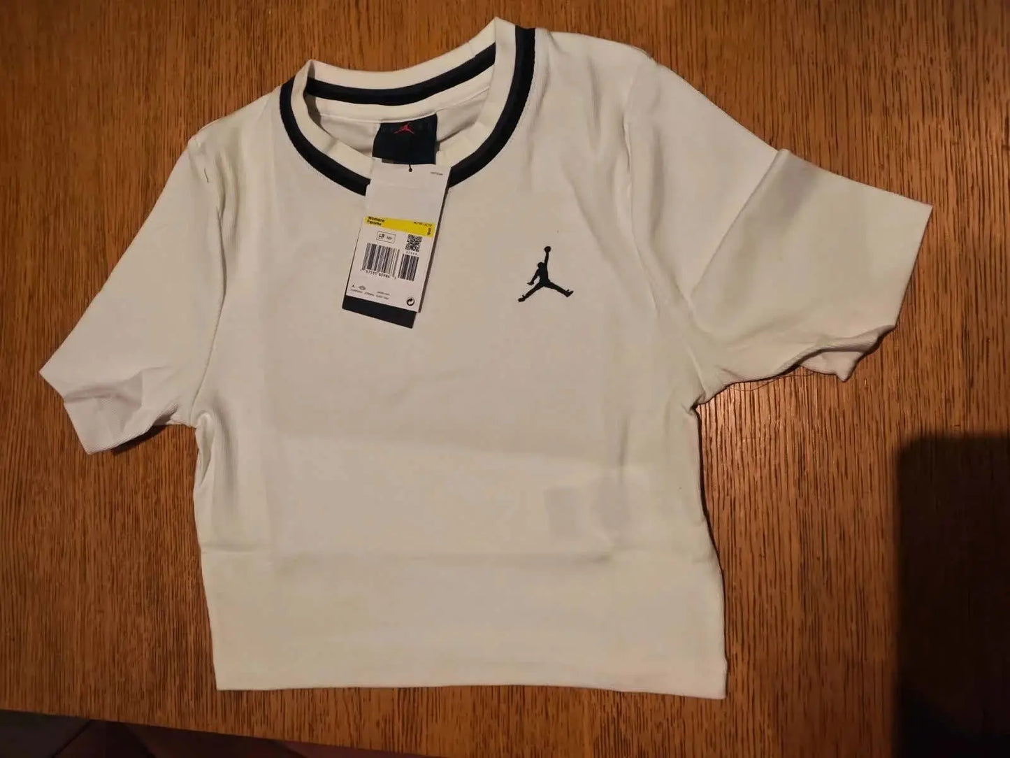 Crop top blanc de Jordan, avec logo brodé et détails contrastés noirs au col et aux manches courtes.