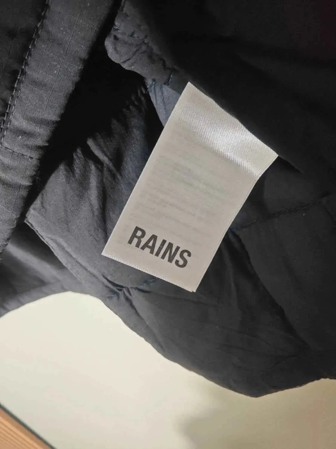 Veste matelassée marine de Rains, avec une étiquette blanche portant le logo de la marque.