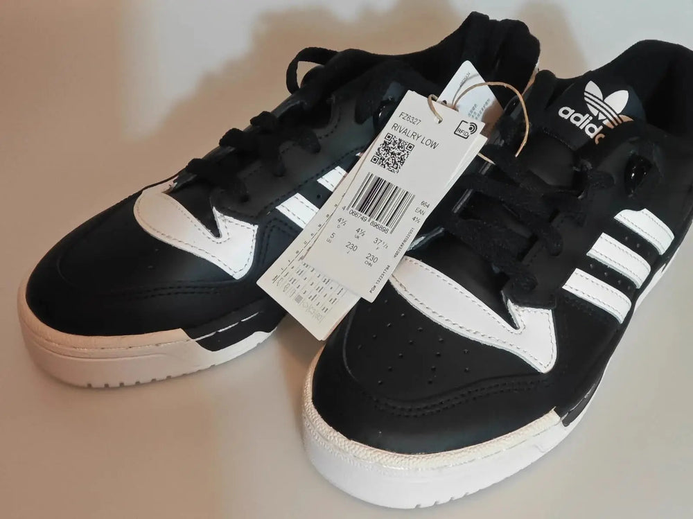 Baskets basses noires et blanches Adidas, avec étiquette attachée.