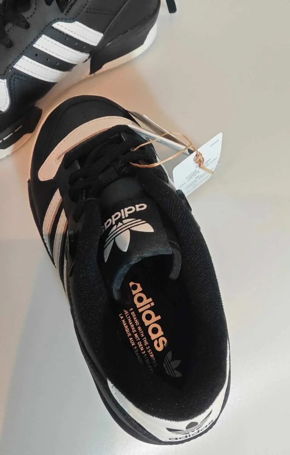 Baskets basses noires et blanches Adidas, avec logo visible sur la languette et l'intérieur.