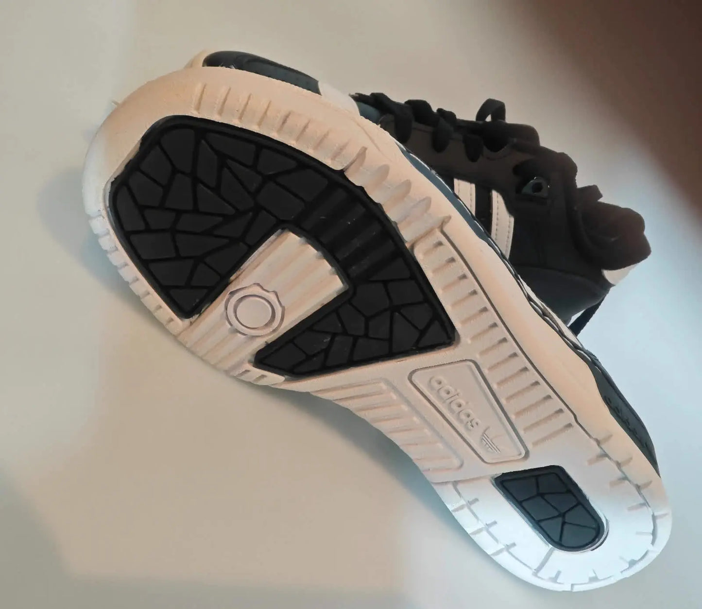 Baskets basses noires et blanches de Adidas, avec semelle texturée noire et blanche visible.
